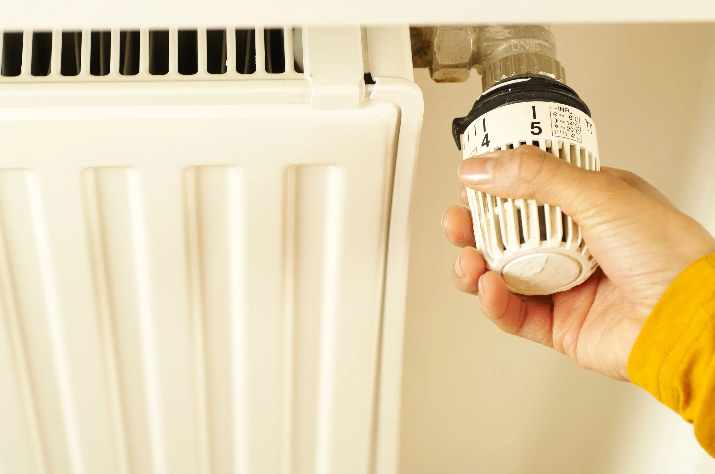 Une main règle la tête thermostatique d'un radiateur blanc